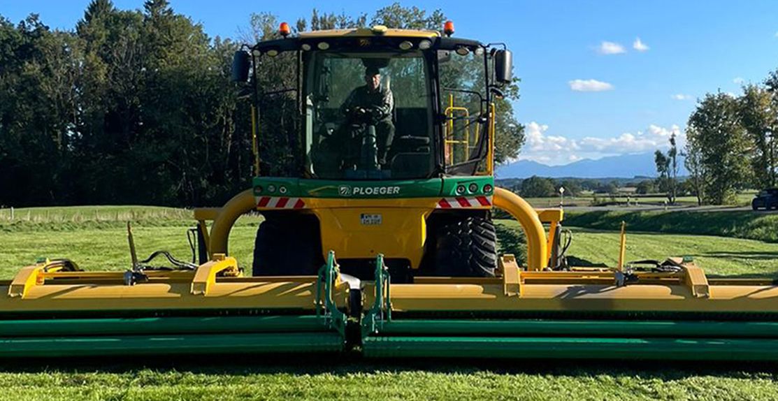 Gelber Ploeger Breitbandmäher bei der Heuernte auf einer grünen Wiese